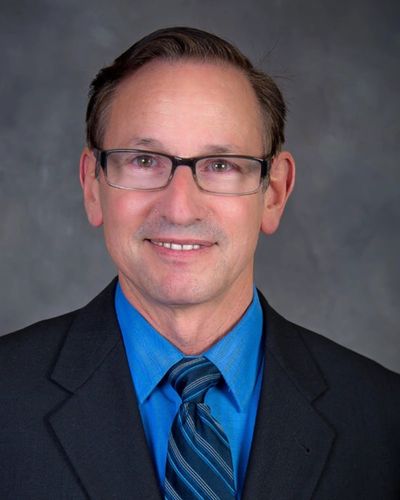image of a man wearing gasses in navy suit with blue shirt and tie
