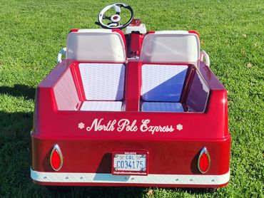 Red North Pole Express vehicle with white seats on grass.