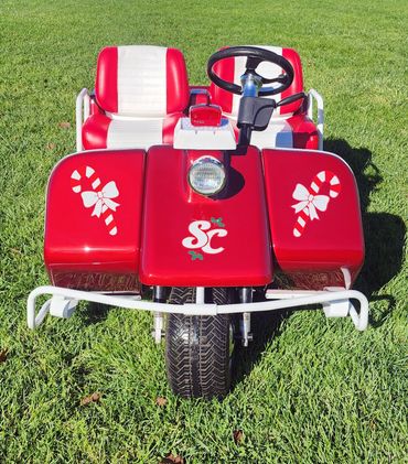 Red and white golf cart with candy cane decals on grass.