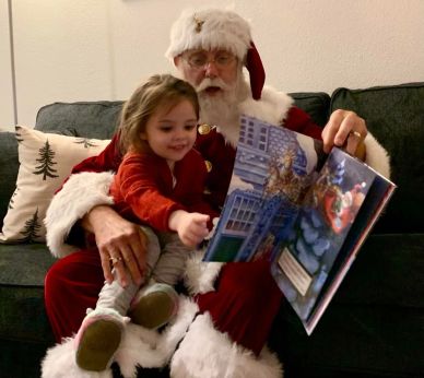 Santa reads a book to a happy child.