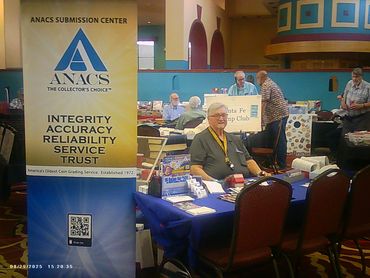 Man sitting at ANACS coin grading service booth at a collector's event.