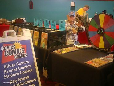 Comic book vendor at a convention with a colorful prize wheel and vintage comics.