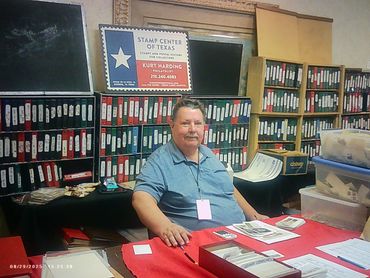 Man sitting at a stamp collector's booth with binders and materials.