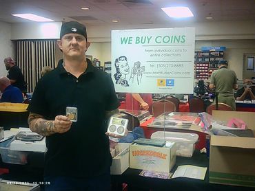 Man in black shirt holding collectible coins at a coin buying booth.