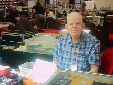 Elderly man selling coins at a collectibles fair.