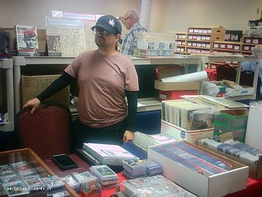 A man standing behind a table full of trading cards and collectibles.