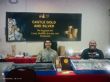 Two men sit behind a coin and bullion buying and selling booth with a Castle Gold and Silver sign.