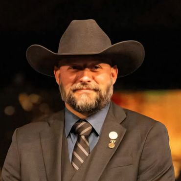 Man in a suit and cowboy hat with a beard and tie.