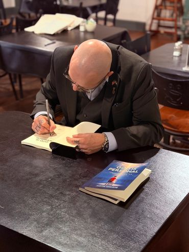 A man in a suit signs a book titled 'God is Personal' by Justin McLane.