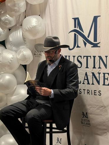 Man in a cowboy hat reading a book at Justin McLane Ministries event.