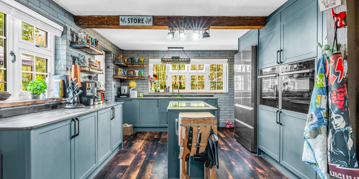 Green cottage kitchen with island, dark quartz worktops, rustic shelves and exposed oak beam.