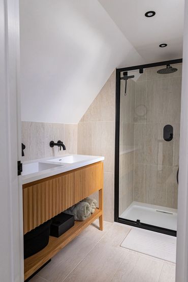 Loft bathroom with a timber-fronted vanity, black taps and glazed shower enclosure.