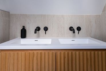 Double basin vanity with a fluted timber front and black wall-mounted taps.