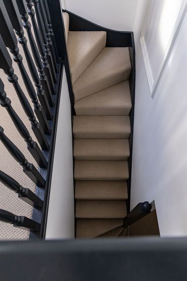 View down the turning loft staircase with carpeted steps and dark timber balustrade.