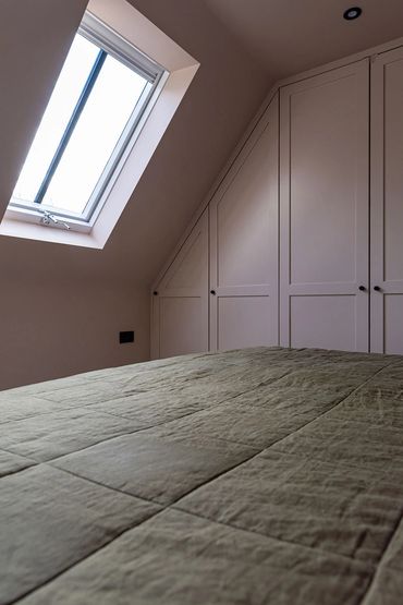 Loft bedroom showing the bed, rooflight and fitted cupboards beneath the roof slope.