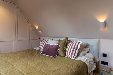 Finished loft bedroom with bedside wall lights, fitted storage and a sloping ceiling.