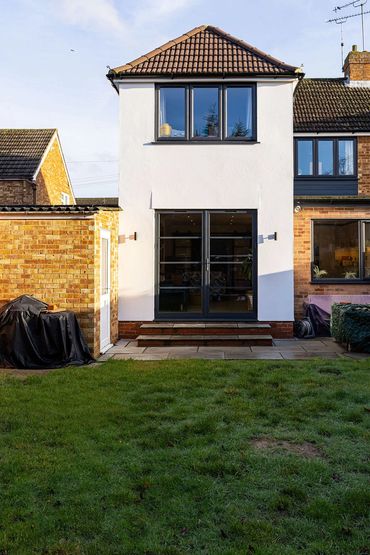 Garden view of the two-storey extension with a tiled roof, white render and dark glazing.