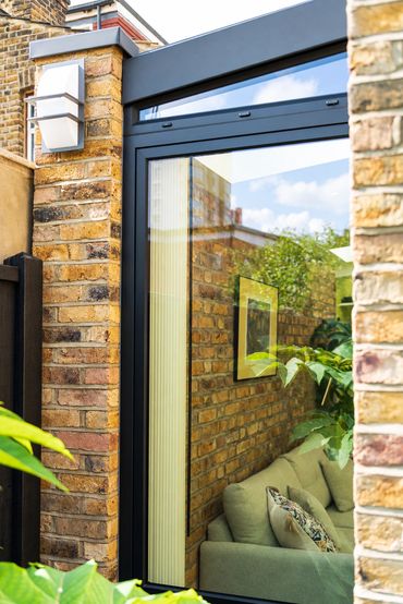 Reclaimed brick pier with an outdoor wall light beside black-framed glazing in Newham.