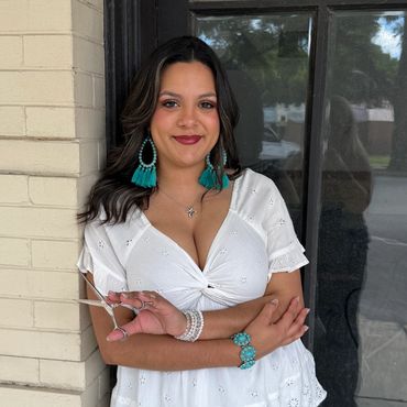 Woman in white blouse and blue jeans holding scissors, leaning against a brick wall.