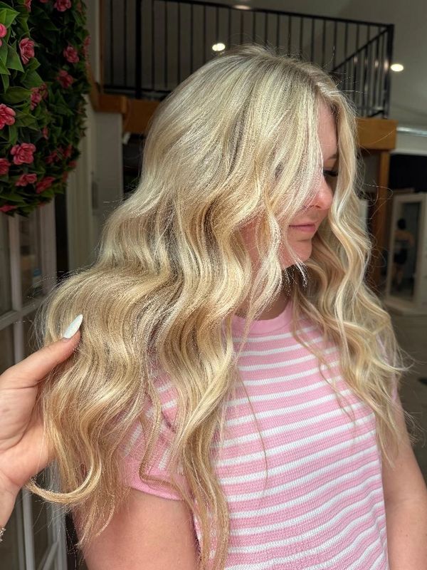 Woman with long, wavy blonde hair wearing a pink and white striped shirt.