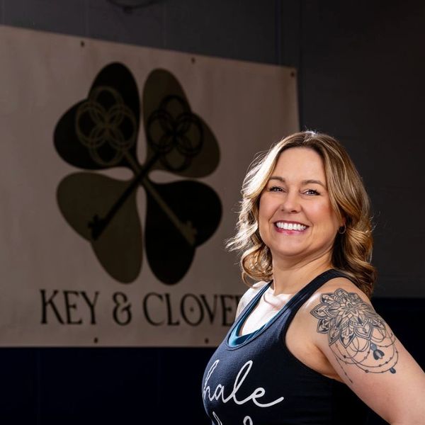 Smiling woman with a floral tattoo on arm in front of a Key & Clover sign.