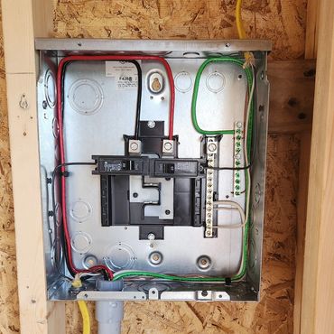 Open electrical breaker panel with wires inside a wooden frame.