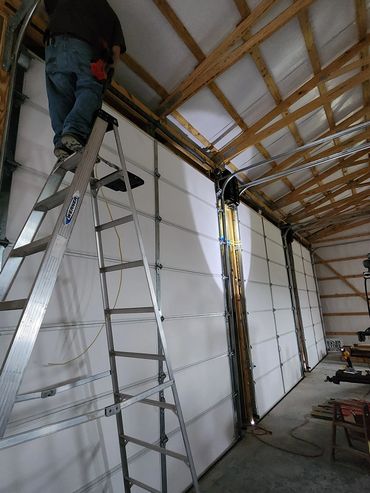 Person working on a ladder by garage doors.