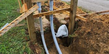 Wooden structure with plumbing pipes in a trench.