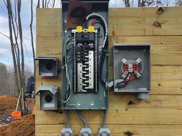 Outdoor electrical panel installed on wooden board at construction site.