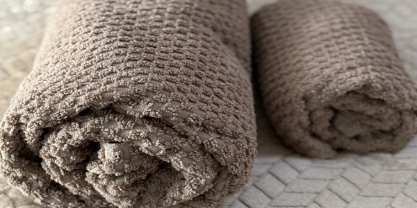 Two rolled brown textured towels on a bed.