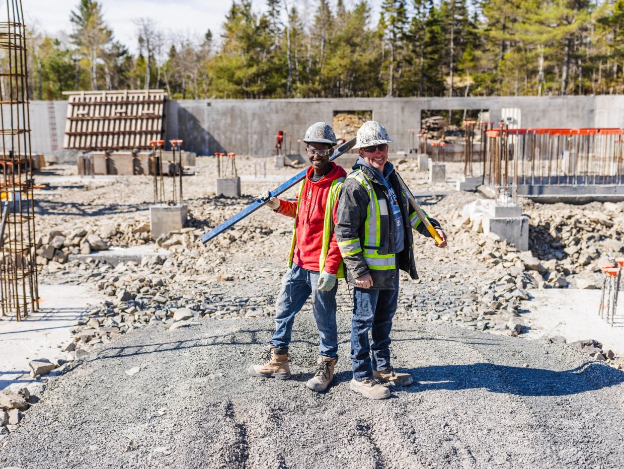 Two construction workers standing back to back, smiling.