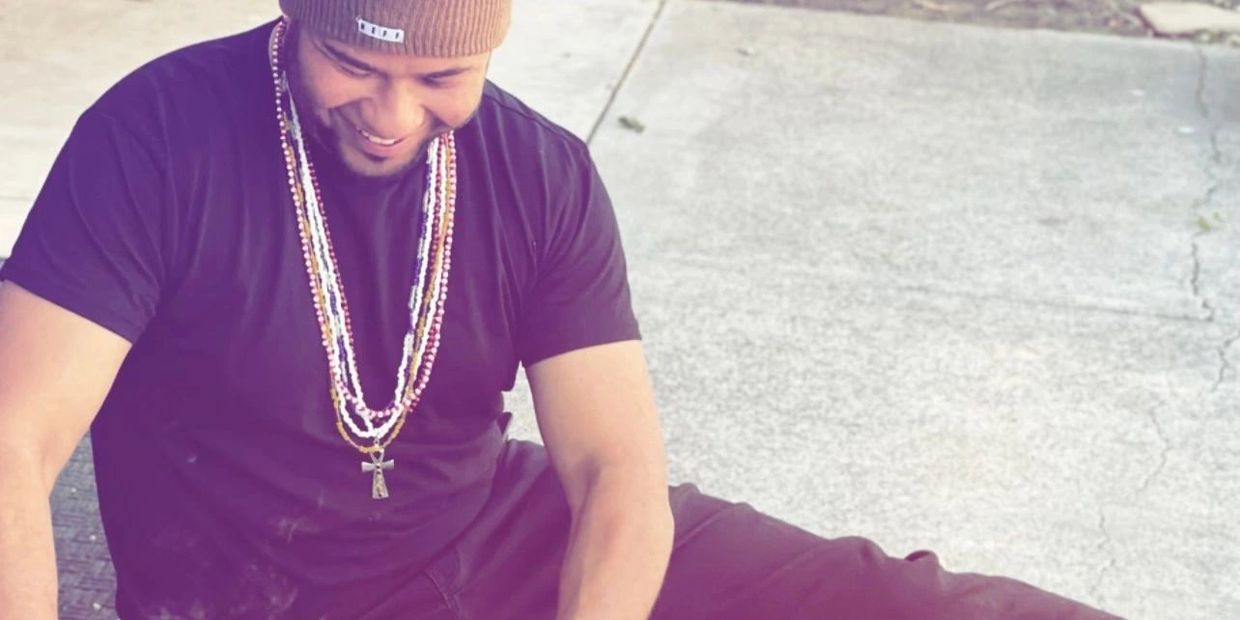 Smiling man wearing a beanie and multiple necklaces.