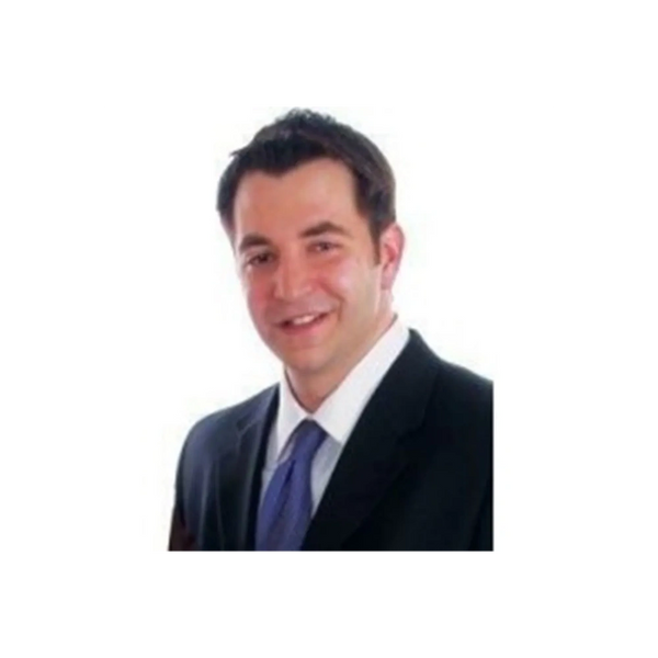 Joseph Najm in a dark suit and blue tie smiling with a white background, dressed professionally.