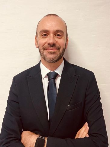 Smiling philip magri in a dark suit and tie with arms crossed.