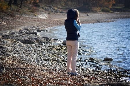Person in winter coat on stoney beach looking out toward the water