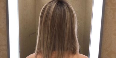 Woman with shoulder-length blonde hair standing in front of a mirror with bright lights.