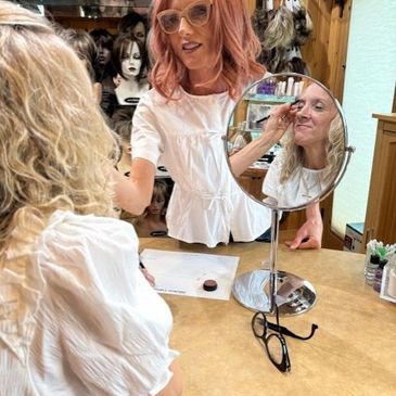 Woman applying makeup while looking in a mirror at a salon.