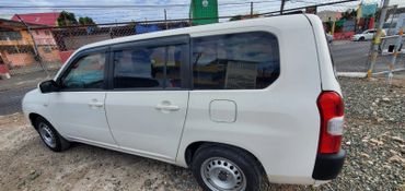 White compact van parked on gravel near a chain-link fence.