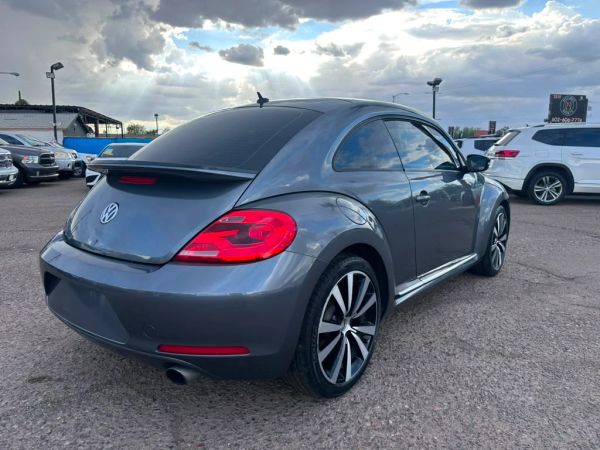 Gray Volkswagen Beetle parked outdoors under a cloudy sky.