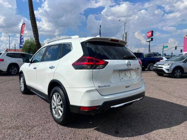 White Nissan Rogue parked in a lot under a cloudy sky.