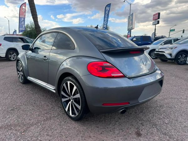 Gray Volkswagen Beetle parked in a lot under a cloudy sky.