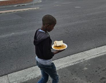 A boy walks on the street holding a plate with bread and soup.