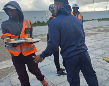Workers in safety vests distributing food outdoors on a cloudy day.