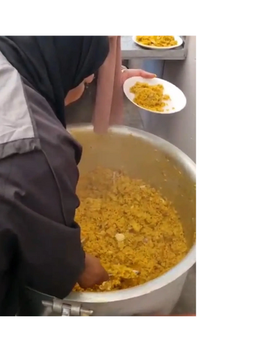 Person serving yellow rice from a large pot into a plate.
