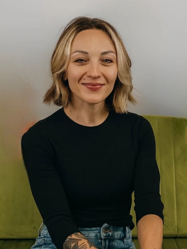 Smiling young woman in black top sitting on a green couch.