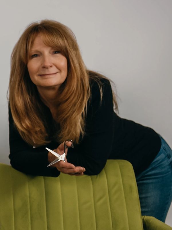 Woman leaning on green chair holding scissors.
