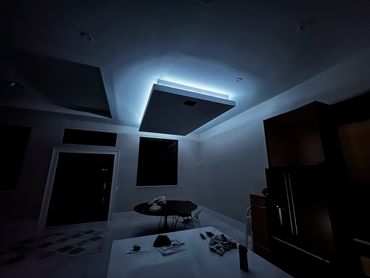 Dimly lit modern room with a glowing ceiling feature and scattered items on tables.