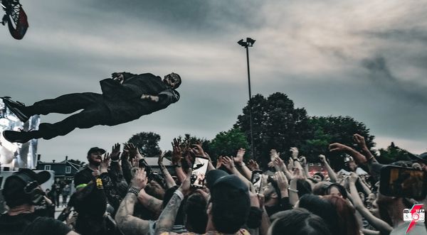 A person crowd surfing at an outdoor event with a cloudy sky.