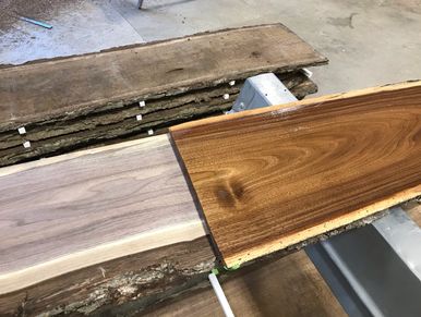 Stack of rough cut live edge walnut boards next to planed boards next to a finished board.