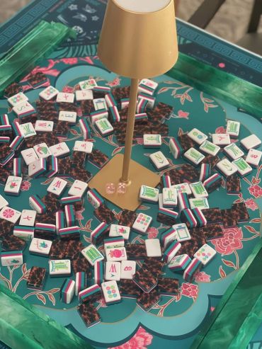Mahjong tiles scattered on a decorative game table with a central golden lamp.